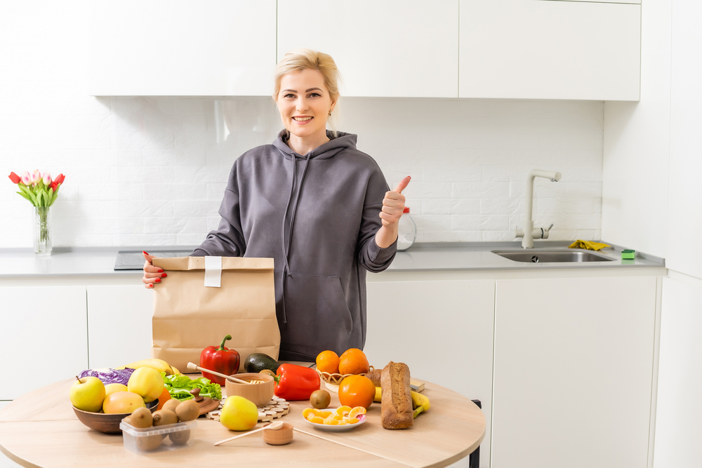 Woman showing off her meal kit subscription box in her kitchen.