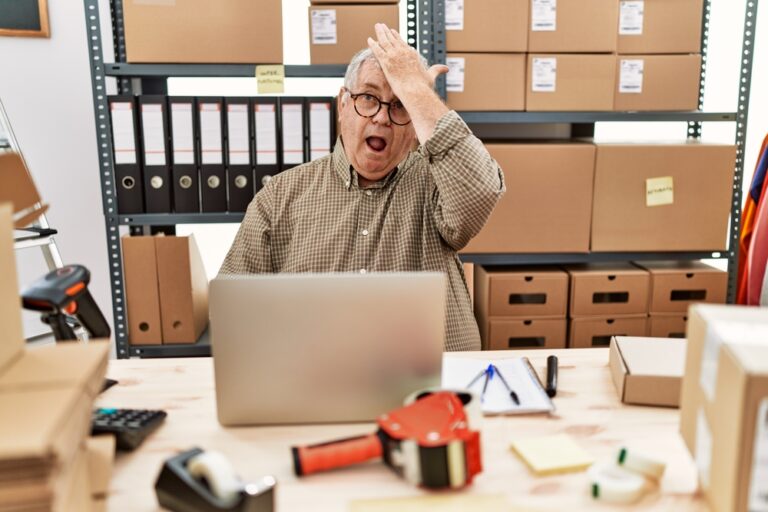 Man working at small business ecommerce with laptop surprised with hand on head for mistake