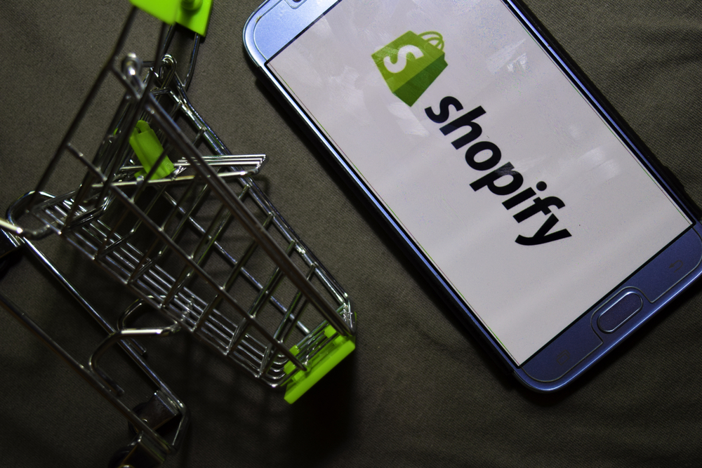 Shopify logo on a mobile phone beside a miniature shopping cart