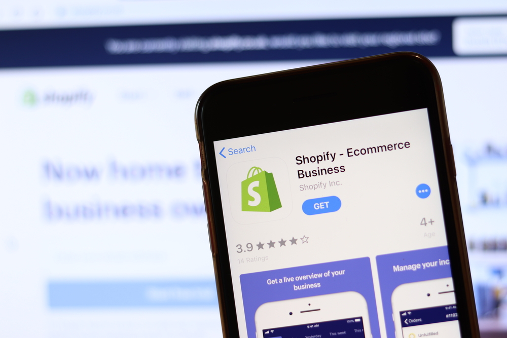 Phone with Shopify icon on screen close up with blur website on laptop. Los Angeles, California, USA - 30 November 2019, Illustrative Editorial