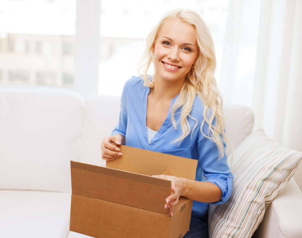 Happy customer sitting on her couch opening a package.